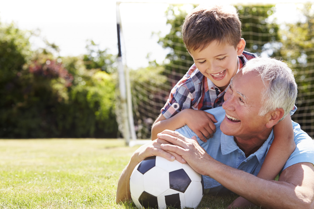 Älterer Mann und Junge spielen gemeinsam Fußball im Garten.
